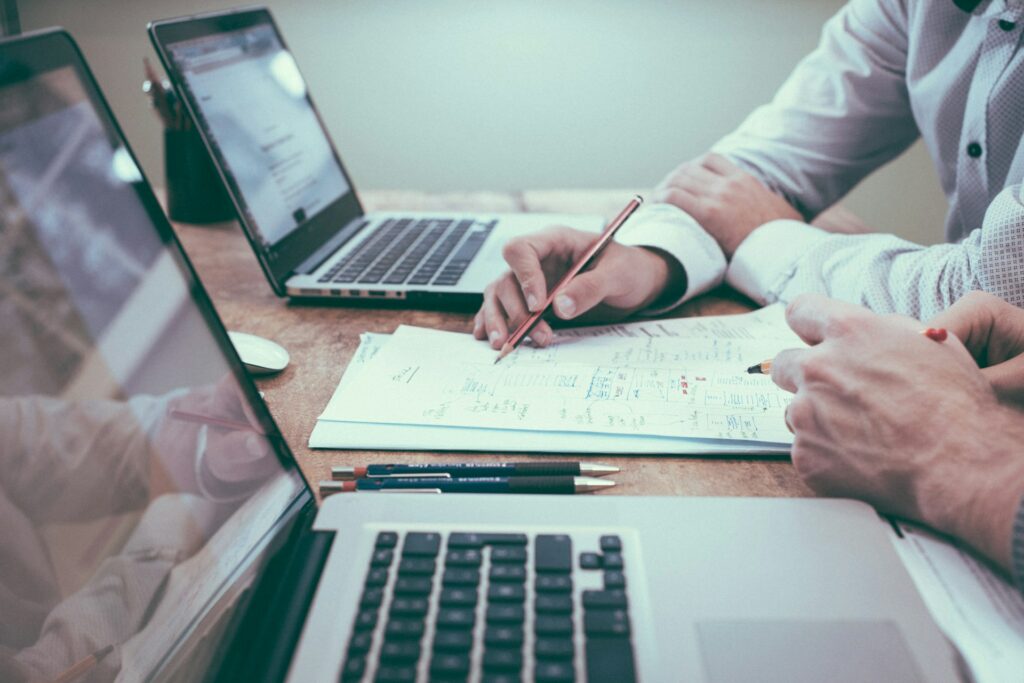 deux personnes dont on voit les mains posées sur un bureau. Elles travaillent sur un audit flash grâce à des ordinateurs portables et des documents.